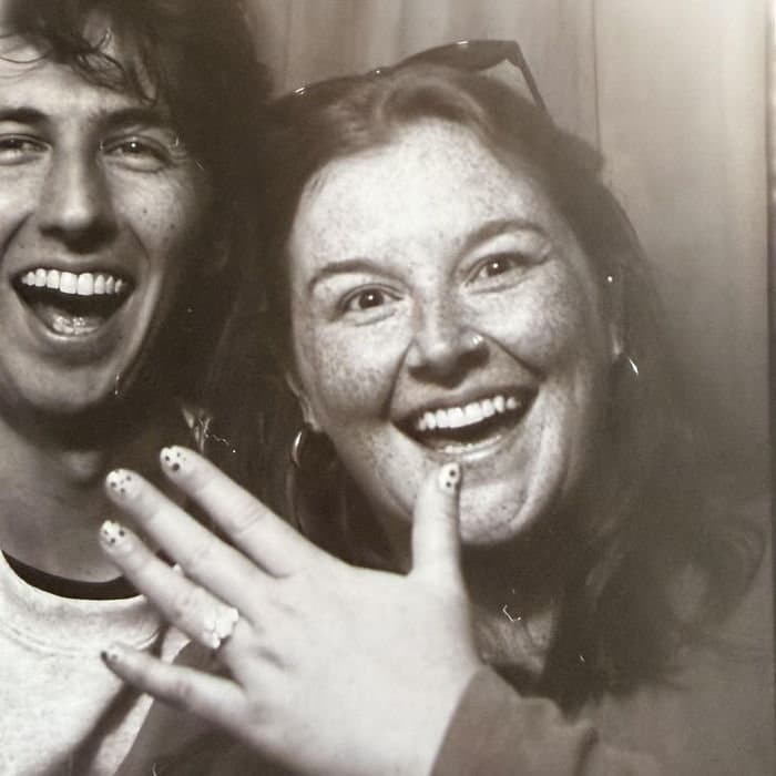 Megan laughing and showing off her engagement ring next to Devin